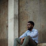 Black man sitting against an urban wall in Ogun State, Nigeria.