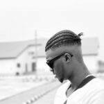 Black and white outdoor portrait of a man with braids and sunglasses in Sagamu, Nigeria.