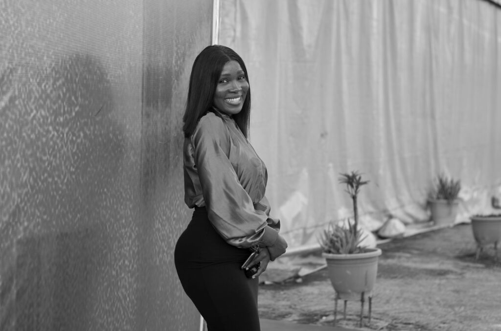 A stylish woman smiling confidently in a black and white outdoor portrait.